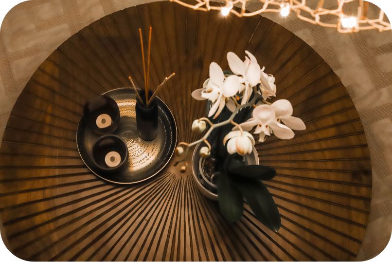 Loungen pyöreä puinen sohvapöytä, jonka päällä on orkidea, tuoksuöljypurkki ja muutama kynttilä.